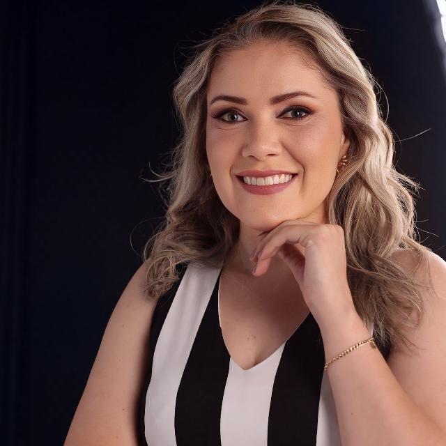 Márcia Denise, sorrindo, com a mão apoiada no queixo